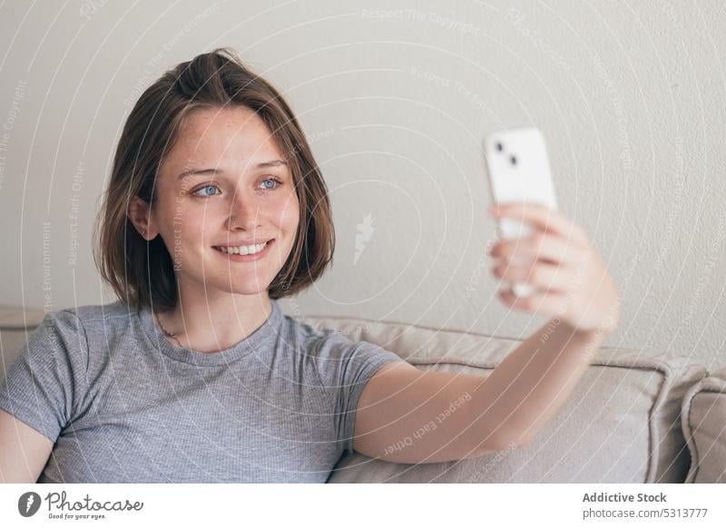 Charming woman taking selfie on smartphone on sofa delight chill home self portrait weekend rest using smile couch happy comfort female glad living room cozy