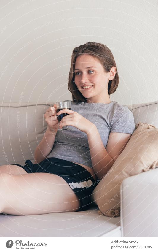 Content woman with cup of coffee on sofa home drink positive smile breakfast rest young female couch happy casual lounge glad beverage domestic content delight