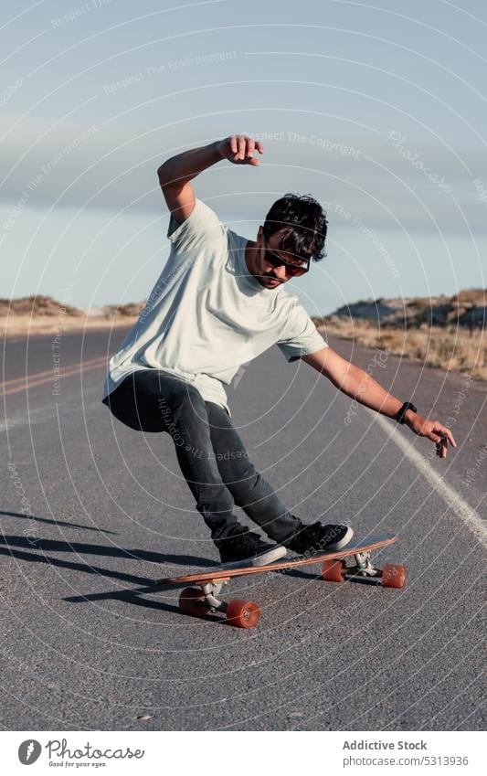 Carefree man balancing on skateboard on asphalt road trick skater ride extreme adrenalin balance activity energy male motion perform hill fast hobby speed skill