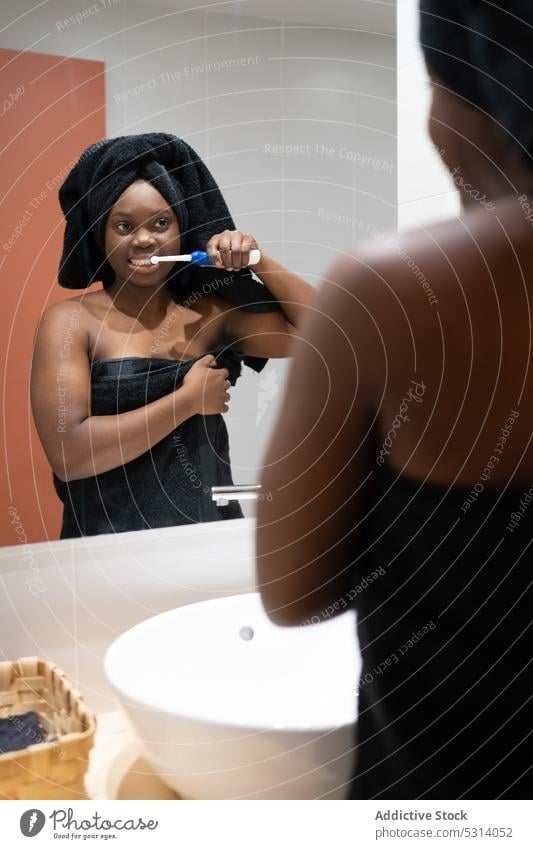 Black woman brushing teeth in bathroom hygiene routine daily procedure mirror sink reflection morning home clean care female african american treat towel