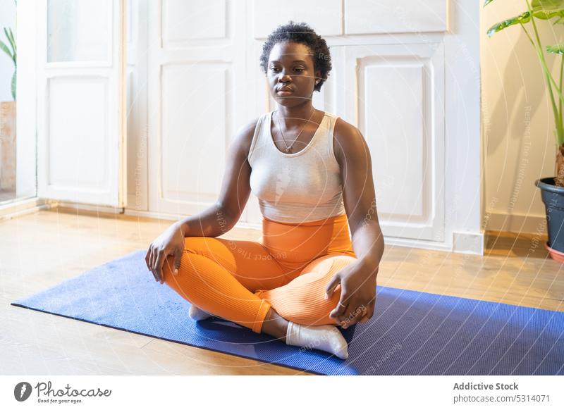 Black woman doing yoga on mat practice lotus pose meditate zen home concentrate sportswear calm padmasana female african american ethnic wellness sit wellbeing