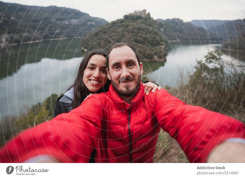 Happy couple taking selfie on lake shore mountain hike smile nature together love trekking hiker travel traveler journey cheerful warm clothes adventure happy