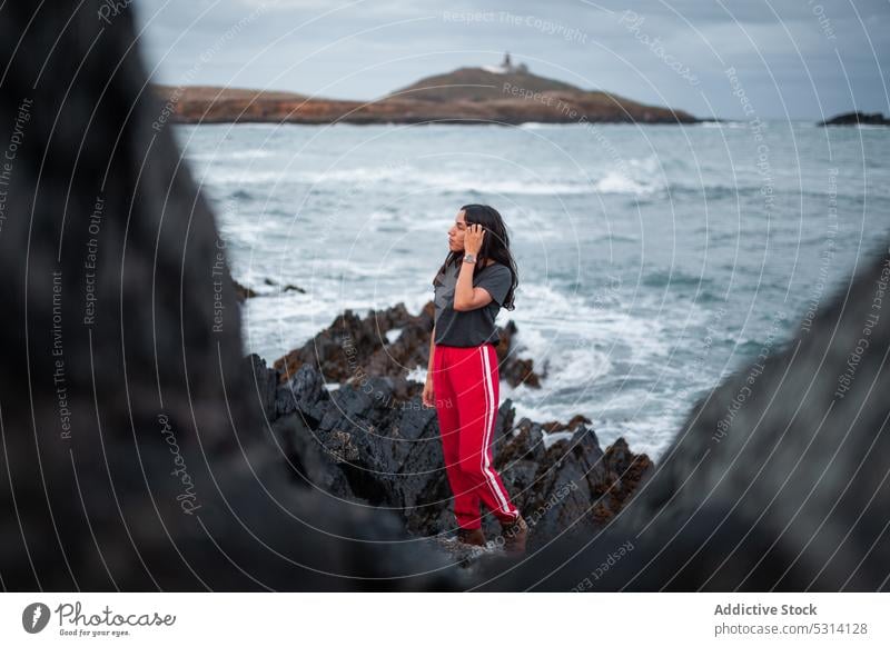 Young woman standing on rock near ocean cliff sea coast mountain nature rocky foam shore ireland sky happy wave female cloudy young water positive admire