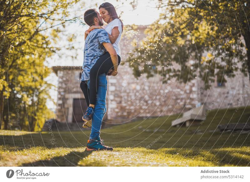Man carrying girlfriend in park on sunny day couple love touch nose romantic relationship date sunlight tree soria spain europe happy smile young boyfriend