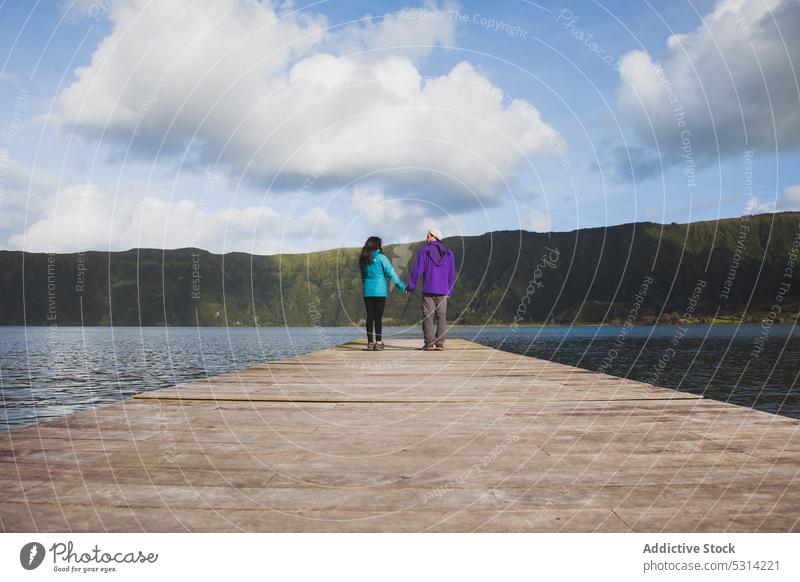 Couple walking along pier of river on cloudy day couple lake admire mountain holding hands landscape wooden relationship picturesque nature azores portugal love