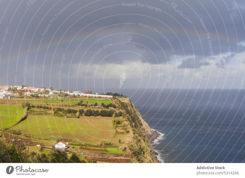 Picturesque scenery of endless ocean near village under rainbow cliff sea cloudy wave picturesque countryside settlement azores portugal island europe sky