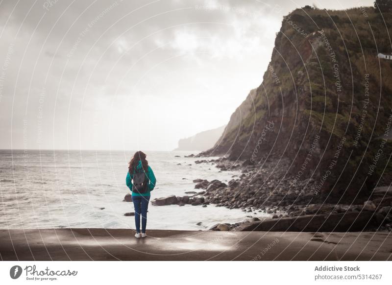 Woman in outerwear admiring ocean on gloomy day woman traveler tourist sea cliff cloudy overcast wet admire female island azores portugal europe beach nature