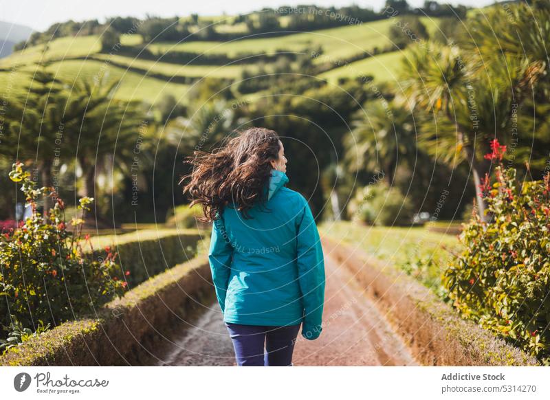 Woman walking along tropical road on sunny day woman traveler tourist path hill exotic tree plant admire female azores portugal europe nature outerwear explore