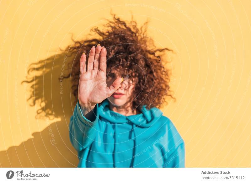 Serious woman showing stop gesture style sign confident demonstrate cool serious female curly hair symbol outfit bright no appearance hoodie colorful caution