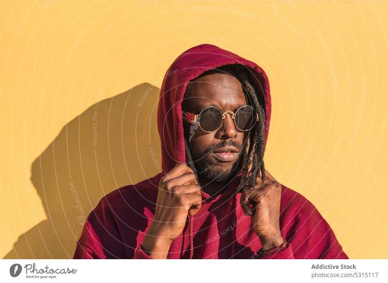 Pensive black man in sunglasses looking away on yellow background thoughtful dreadlocks street style hoodie appearance portrait hipster pensive male serious
