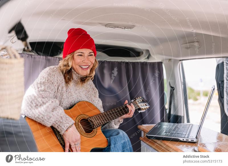 Smiling woman with laptop and guitar play cheerful van musician smile happy instrument device joy young female lifestyle trip guitarist perform online positive