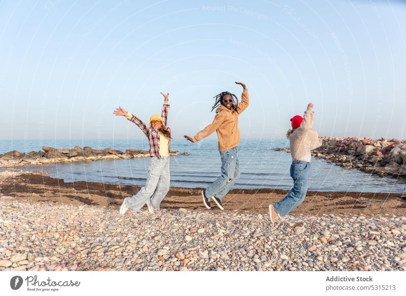 Happy group of diverse friends jumping on seashore women beach having fun happy summer freedom multiracial multiethnic man arms raised girlfriend excited