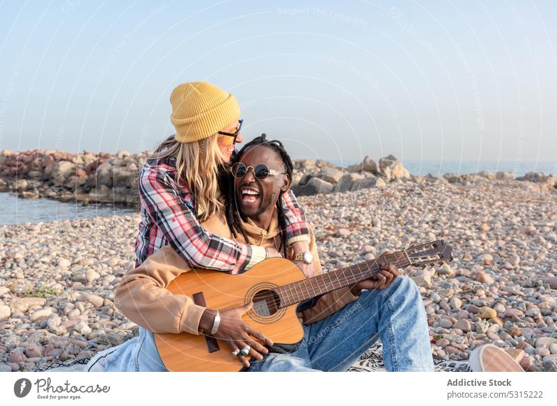Happy diverse friends with guitar on beach man woman play shore summer smile cheerful hug embrace music black ethnic african american sea coast happy weekend