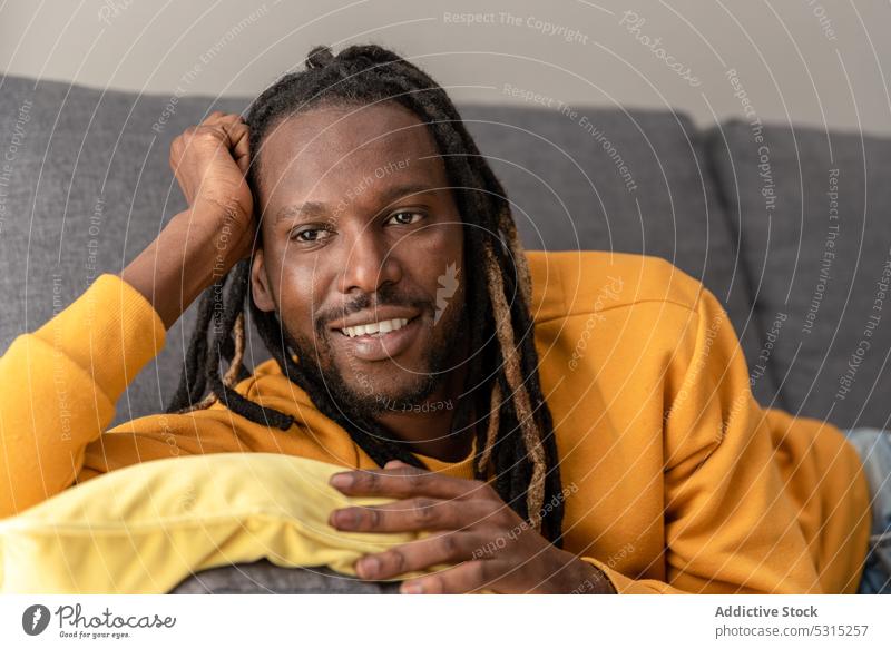 Cheerful black man lying on sofa with pillow smile positive home relax rest weekend cheerful hoodie male happy ethnic dreadlocks chill style bright couch joy