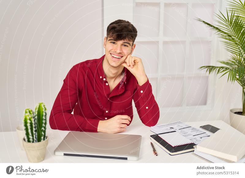 Smiling man with laptop and stationery at table student homework assignment education notebook positive smile study male young learn happy cheerful knowledge
