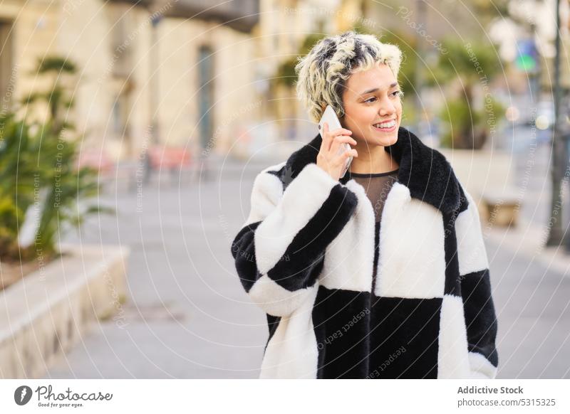 Smiling woman talking on smartphone on street conversation phone call smile speak style happy young trendy coat device cheerful female city mobile gadget