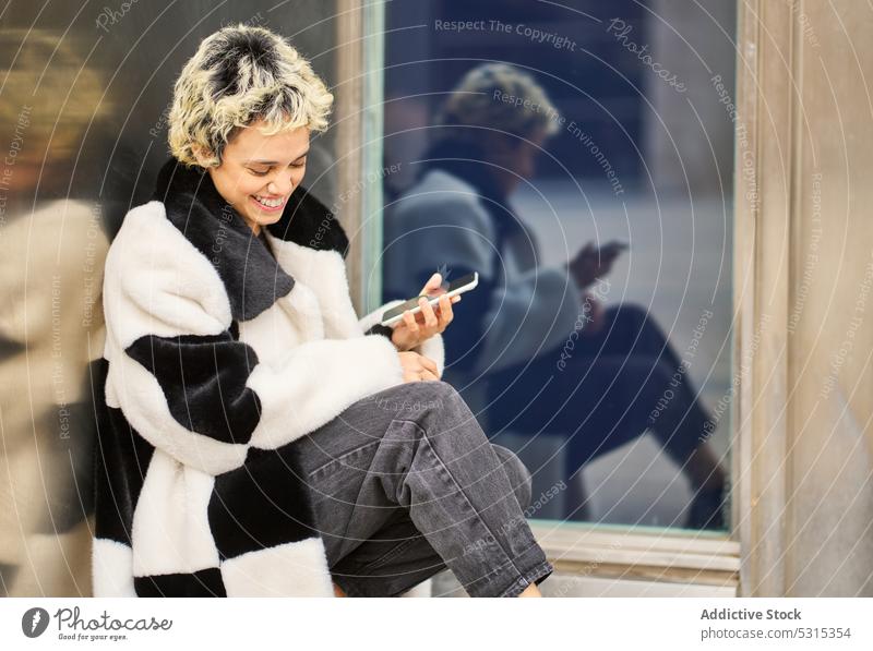 Delighted woman with smartphone on street happy using rest message cheerful building coat female city device browsing surfing gadget mobile warm smile young