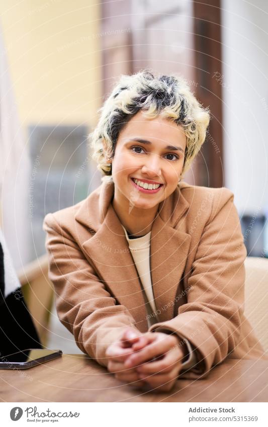 Smiling woman in coat at table on street cafe smile positive cheerful trendy rest terrace female happy young wooden cafeteria enjoy modern delight chill
