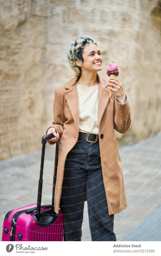 Cheerful woman with suitcase and ice cream on street old smile city style happy eat building cheerful trendy young positive tourist town coat female urban