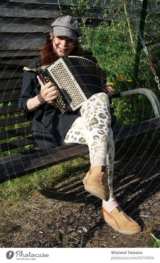 Redhead lady sitting on a bench and playing a diatonic button accordion Face Person Sitting outdoor vintage old outdoors antique traditional shirt caucasian