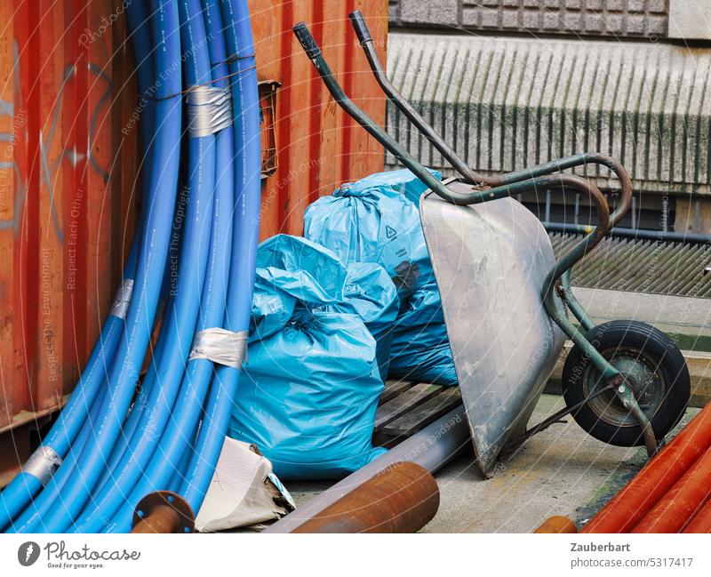 Urban still life of a construction site with wheelbarrow, flexible pipes or hoses, leaning against containers Construction site Wheelbarrow conduit Hose