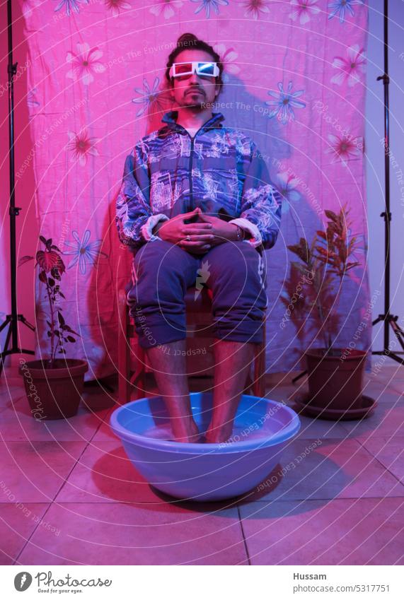 it is a concept photo about a person wearing a 3d glasses and his feet in bucket of water with lighting red and blue. lens optical colorful eyewear entertain
