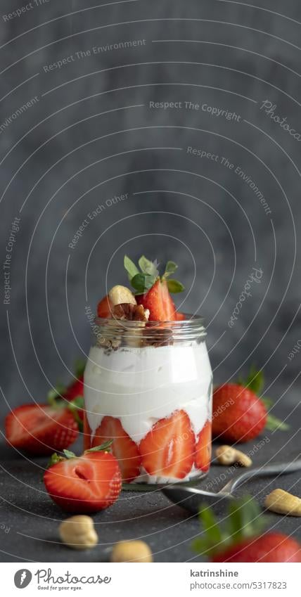 Greek yogurt, nuts and strawberries in a glass jar on grey table with a spoon close up, copy space breakfast Healthy fruits eat protein concrete red food