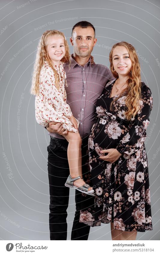 Portrait of a happy family father, pregnant mother, little daughter having fun together isolated over gray background girl holding portrait box present mom kid
