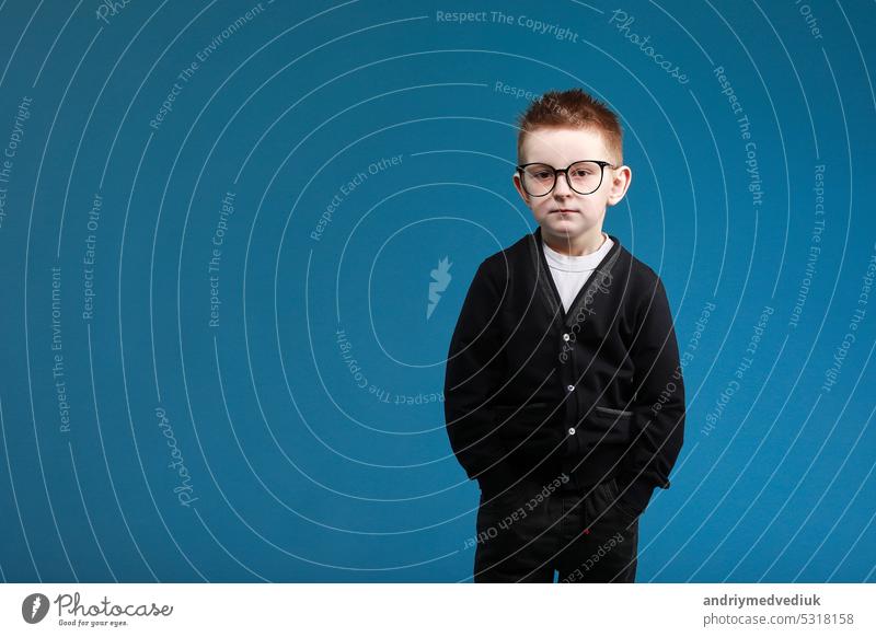 Back to school. Adorable kid in nerdy glasses and school uniform looking at camera while standing against blue background boy child portrait person little
