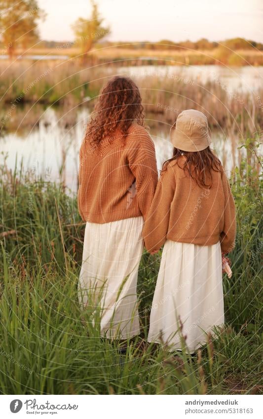 Mother day. Back view of young mom with little girl are standing near lake, pond on summer day. Family enjoying life together. Mother and child daughter spending free time outdoors. Family look.