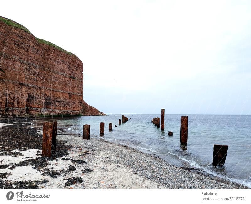 The waters of the North Sea are receding. The low tide comes in. Metal pillars, the remnants of war, emerge from the tides. In the background, the rocks of red sandstone rise into the air.