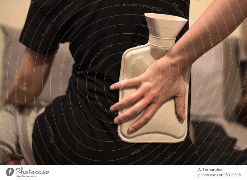 Detail of a woman using a hot water bag on the lower back area to relieve pain through heat therapy bed warmer heater heated female health care Woman Bed