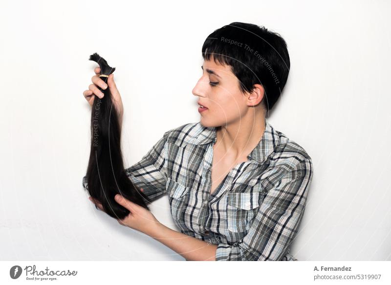 A young woman with short hair shows off a section of hair in a ponytail that she has just cut. Concept of hair donation for cancer patients haircut hair cut
