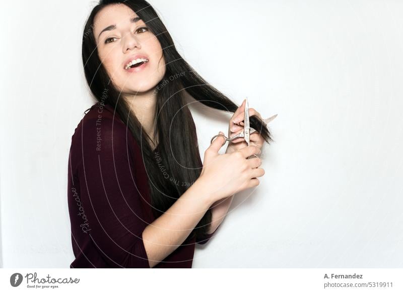 Beautiful joyful young woman cutting with scissors the ends of her long black hair haircut hair cut section section of hair holding chop off Hairdresser