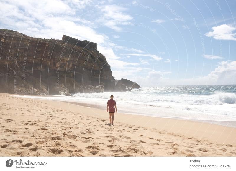 Woman on beach goes to sea Beach Ocean cliff Waves Sand Sandy beach Portugal Nazaré coast Beautiful weather Water Exterior shot Nature Summer Vacation & Travel