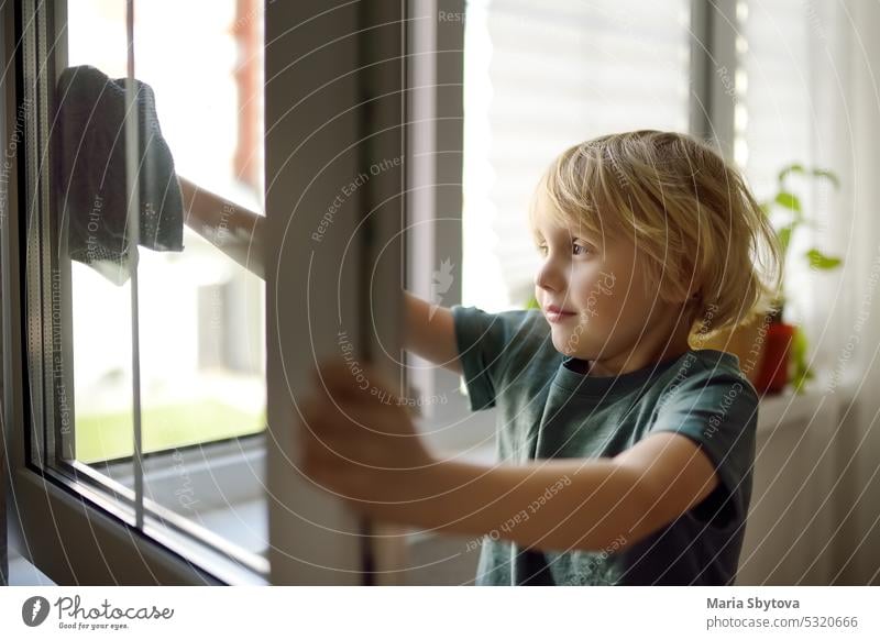 Cute little boy washing a window at home. Child helping parents with household chores, for example, cleaning windows in his house. Children doing housework.