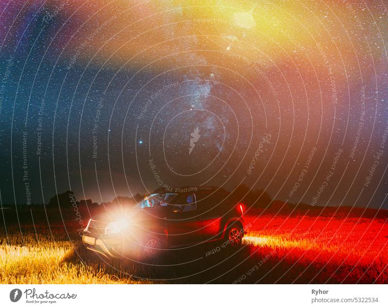Agricultural Colorful Background Copy Space. Night Starry Sky Above Rural Landscape With Suv Parked On Field Meadow After Harvest. Glowing Stars And Sunset Lights
