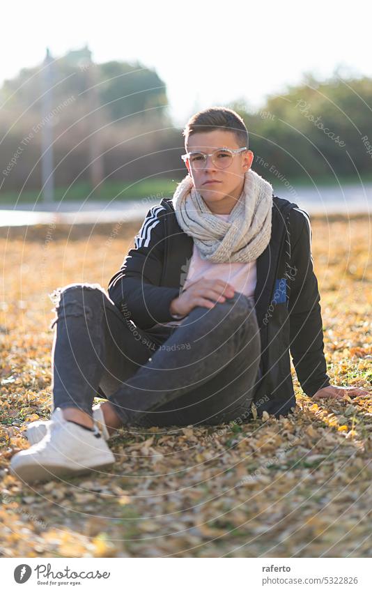 Portrait of teenager with glasses sitting on the ground in a park, looking at the camera. portrait male street young man boy youth casual attire lifestyle guy