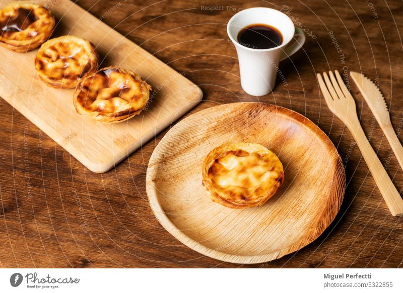Pasteis de nata, a typical sweet from Lisbon, Portugal, a cake on a plate next to a cup of coffee, in the background several more cakes. pasteis de nata dessert