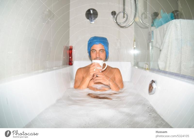photo about a guy in bathtub relaxing and drinking cup of tea wearing a plastic bag on his head taking a bath leisure fun luxury home bathroom lifestyle enjoy