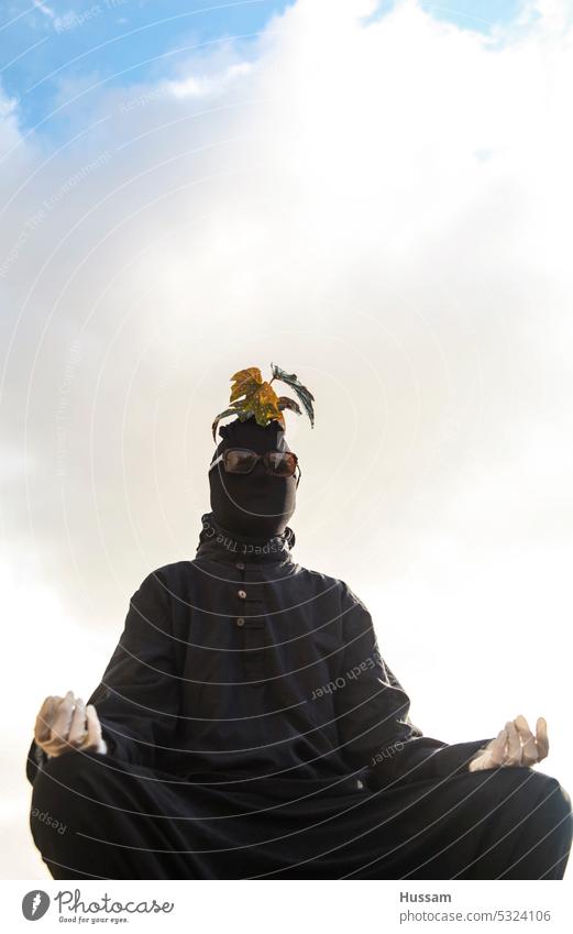 photo concept about a person In meditation pose, covered in black clothes and plant on his head and wearing white gloves spirituality position relaxation yogi