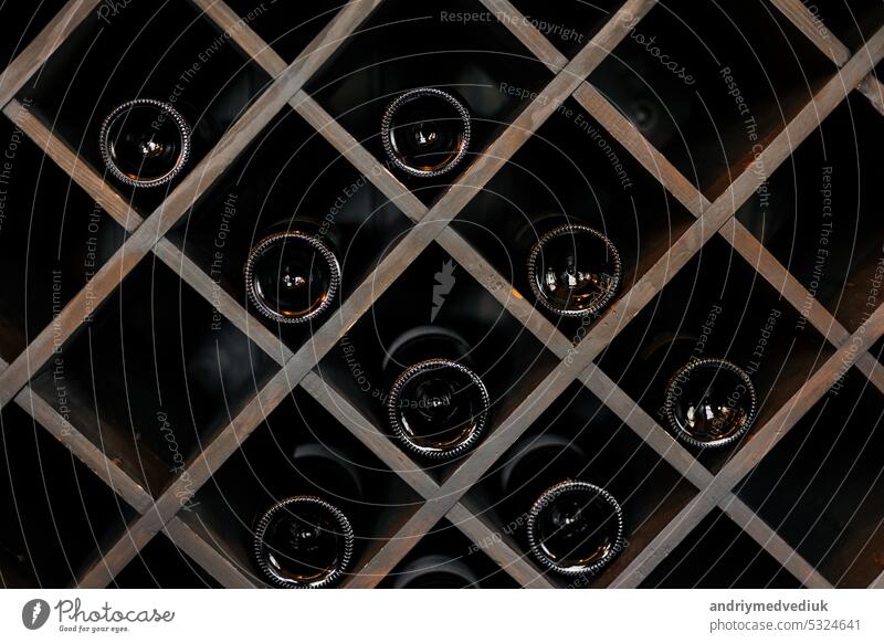 Elite dark glass wine bottles stacked on wooden racks in cellar, market, restaurant or home. Collection of bottles wine at shelf alcohol drink storage