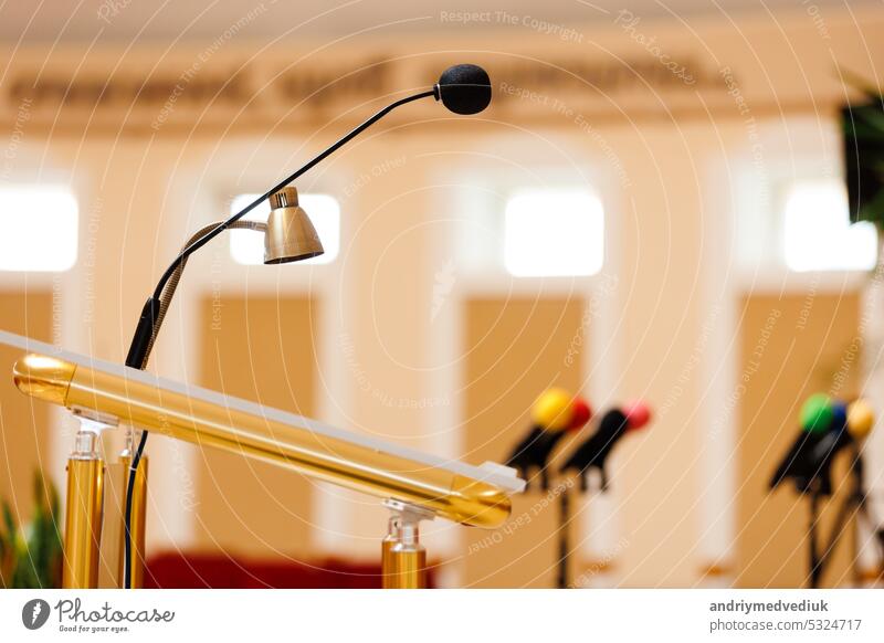 Selective focus of a microphone with other colorful microphones on podium blurred in the background. Concept of communication, media, press conference, event, performance, politics, company.