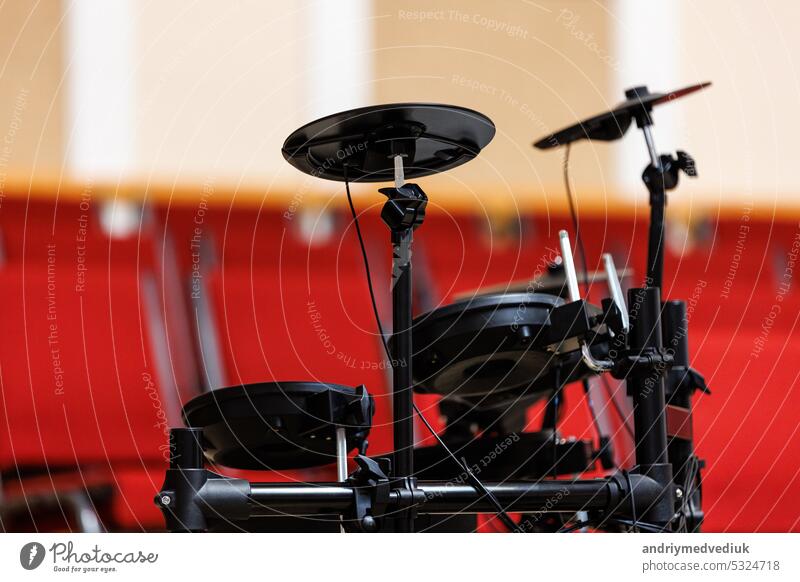 electronic drum set on podium, a lot of red chairs blurred in the background. Concept of concert, event, communication, seminar, media, graduation, performance
