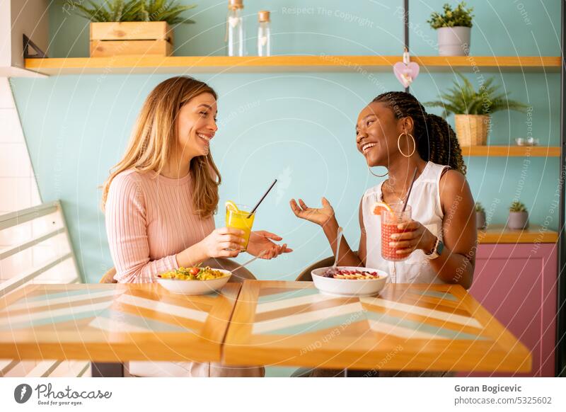 Young black and caucasian woman having good time, drinking fresh juices and having healthy breakfast in the cafe african african female attractive beautiful