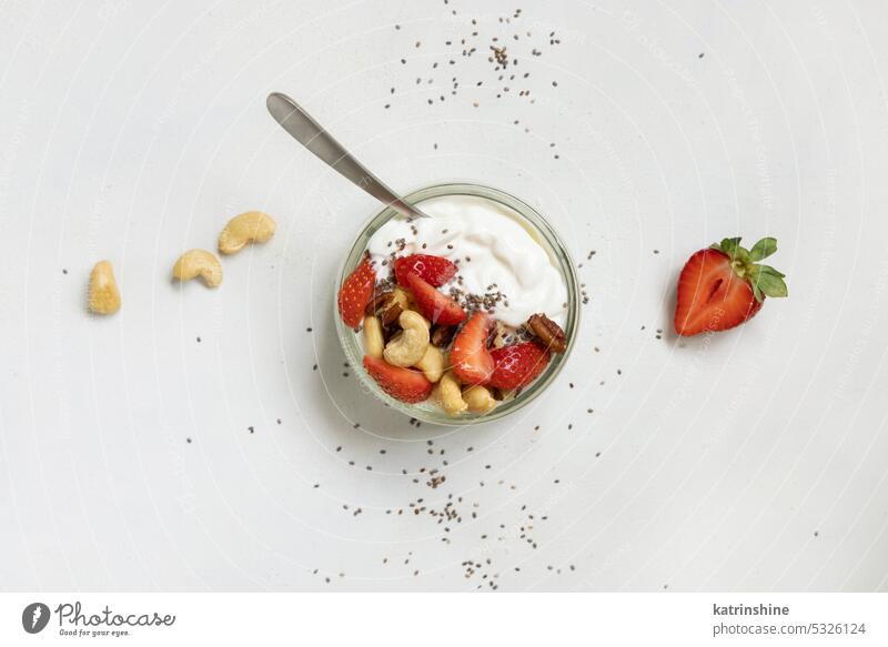 Greek yogurt, nuts and strawberries in a glass jar with a spoon on a white table top view breakfast copy space Healthy fruits eat protein red food organic