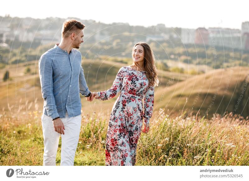 Young couple is hugging and walking in summer field with grass on the background town. Man and woman. Concept of lovely family. beautiful young sun romantic