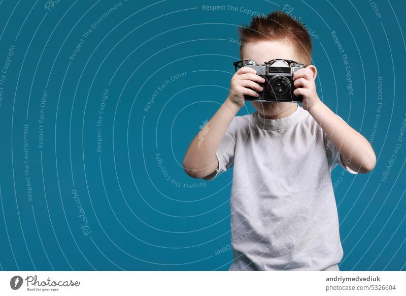 Little boy taking a picture using a retro camera. Child boy with vintage photo camera isolated on blue background. Old technology concept with copy space. Child learning photography