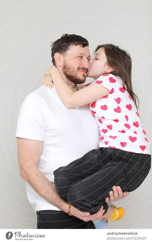 young dad holds his little daughter in his hands. father hugging his child with love and child kiss him. man in white t-shirt and girl in t-shirt with red hearts. Happy Father's Day. valentine's day