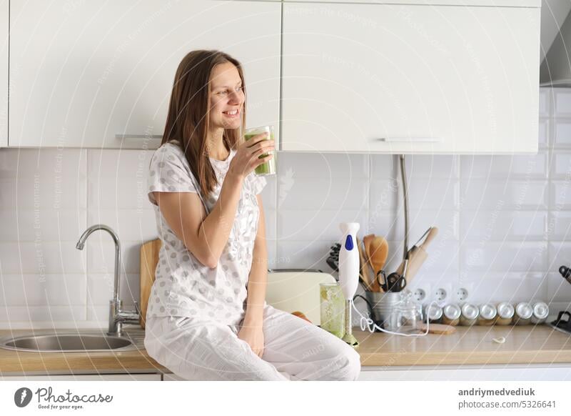 Beautiful girl drinks freshly prepared smoothie in kitchen. smoothies freshly made from assorted vegetable ingredients on kitchen counter. Healthy Eating. selective focus